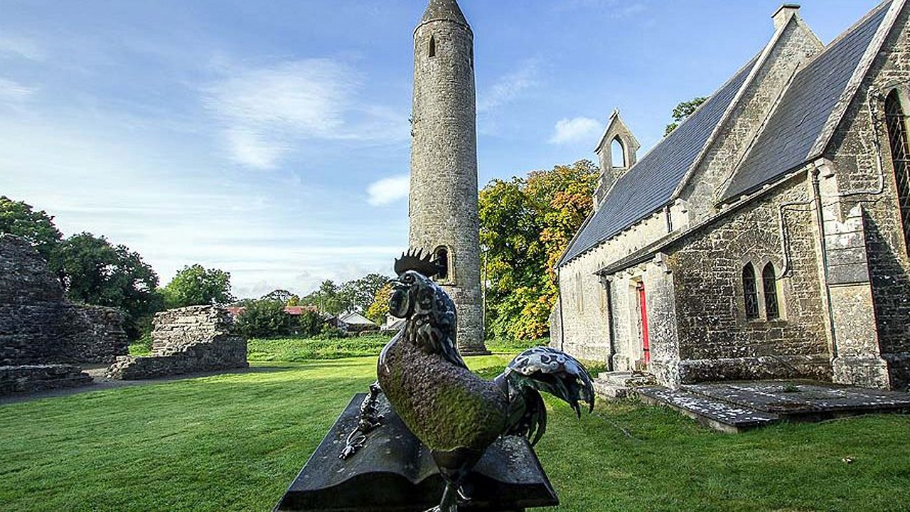 Photo of Timahoe round tower with Rooster sculpture